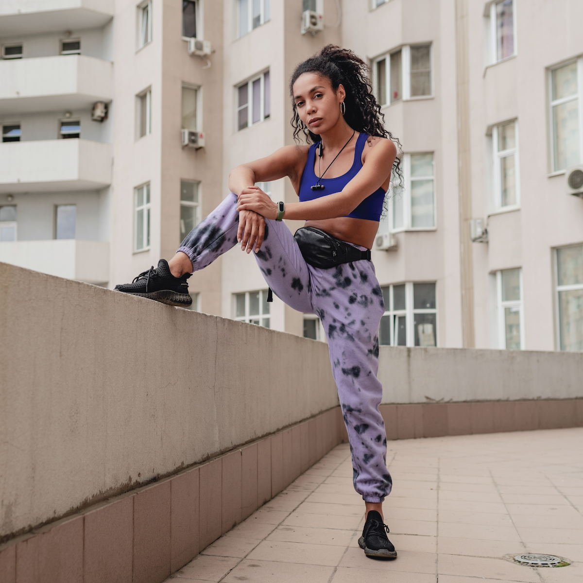 A young woman in tie dye joggers practicing HRV techniques while leaning against a wall.
